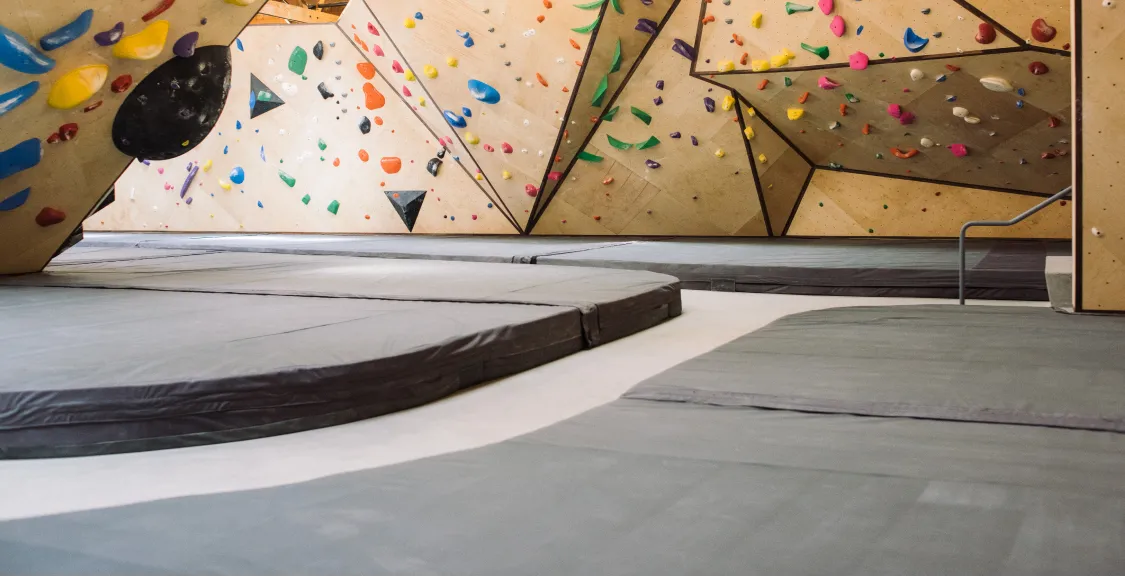 Bouldering floor pads beneath curved birch climbing walls